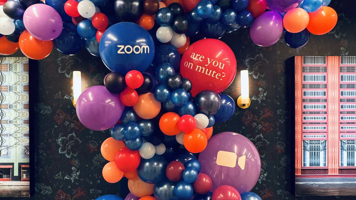 Close view of a balloon installation for Zoom in New York City by Alaric Flower Design: a Zoom-branded balloon, an "are you on mute?" balloon and a camera-icon balloon set into an organic garland.