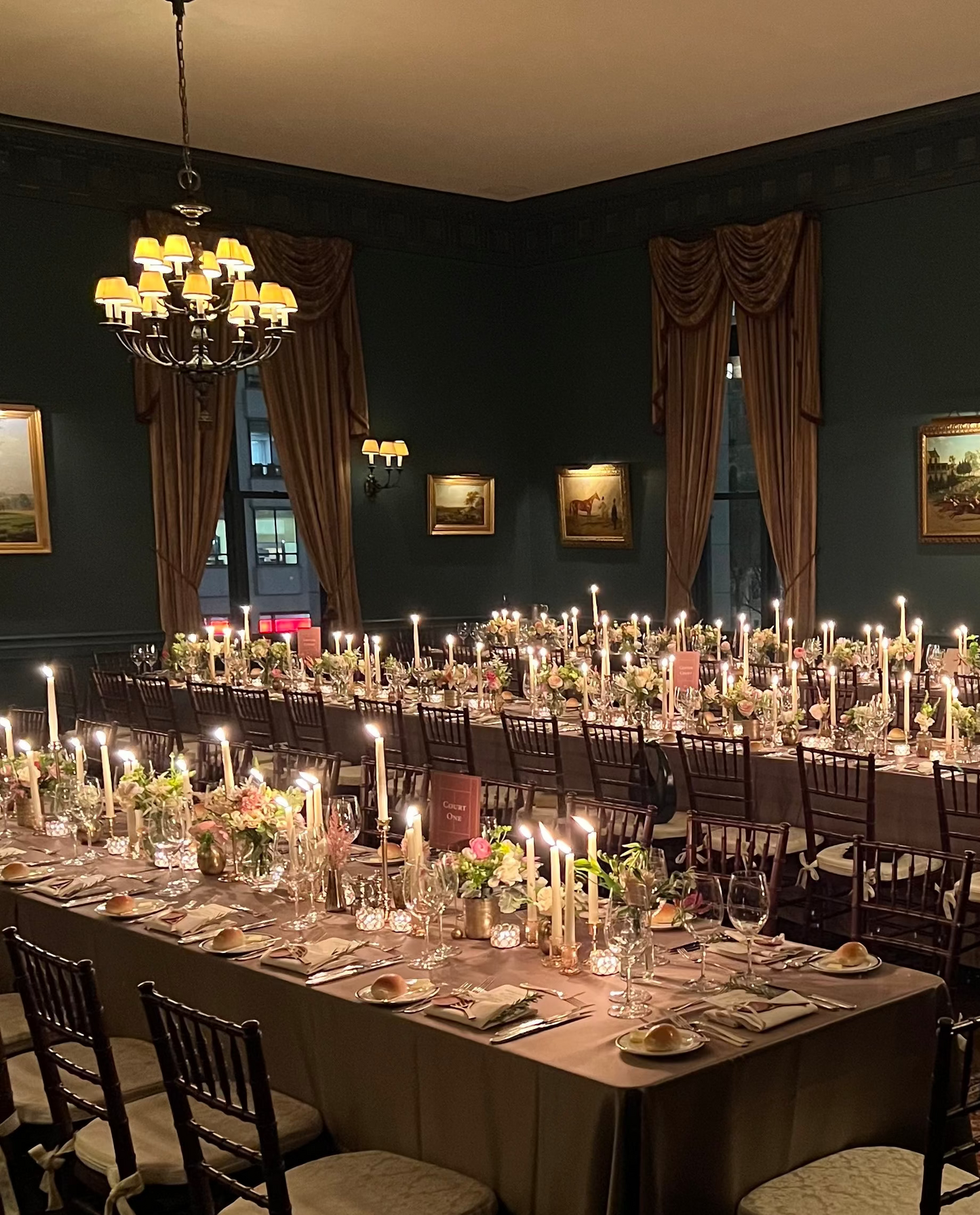 Dining room with long tables set for a formal dinner, candles lit, and elegant decor.