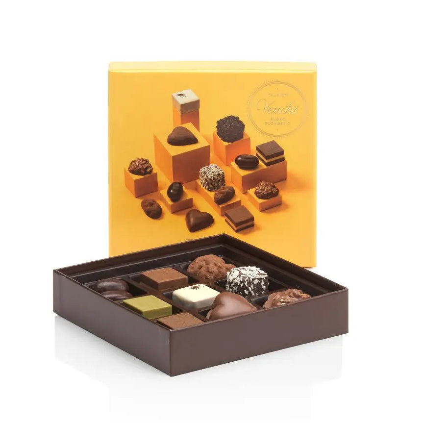 Assorted chocolates in a brown box with a yellow lid on a white background