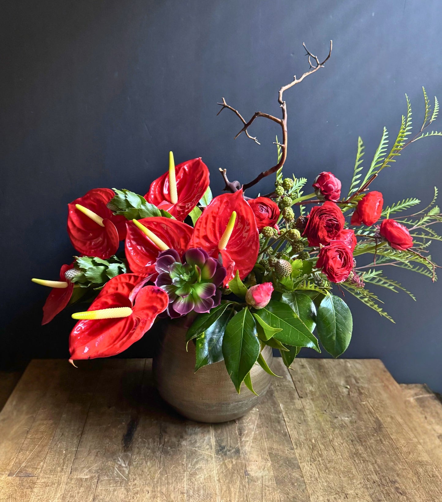 Floral arrangement with red flowers and green leaves in a vase on a wooden surface.