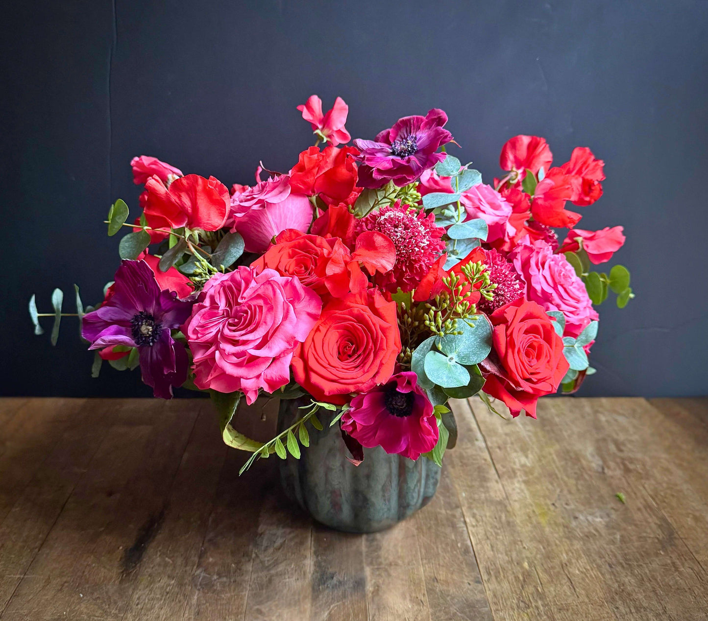 Bouquet of colorful flowers in a vase on a wooden table with a dark background