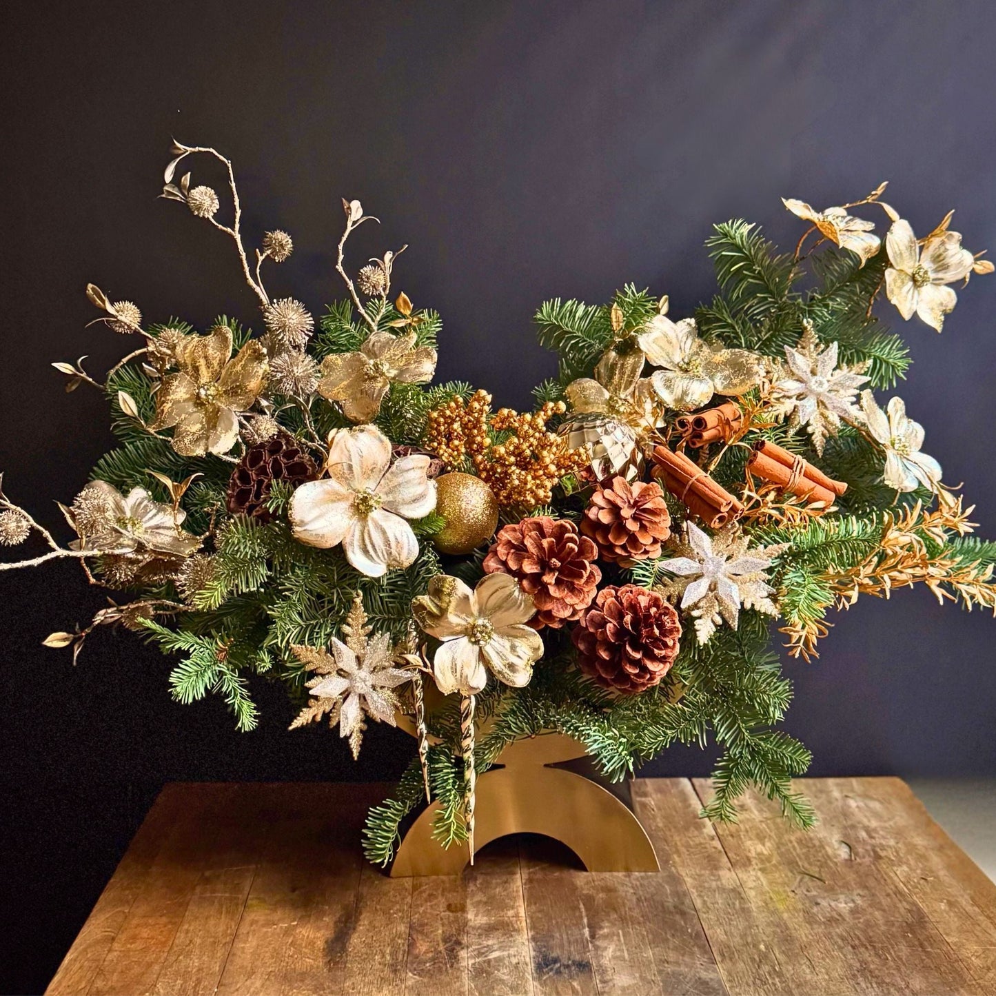 Alaric Flowers NYC opulent holiday centerpiece with gilded magnolia, metallic stems, pinecones & evergreens in gold vase.