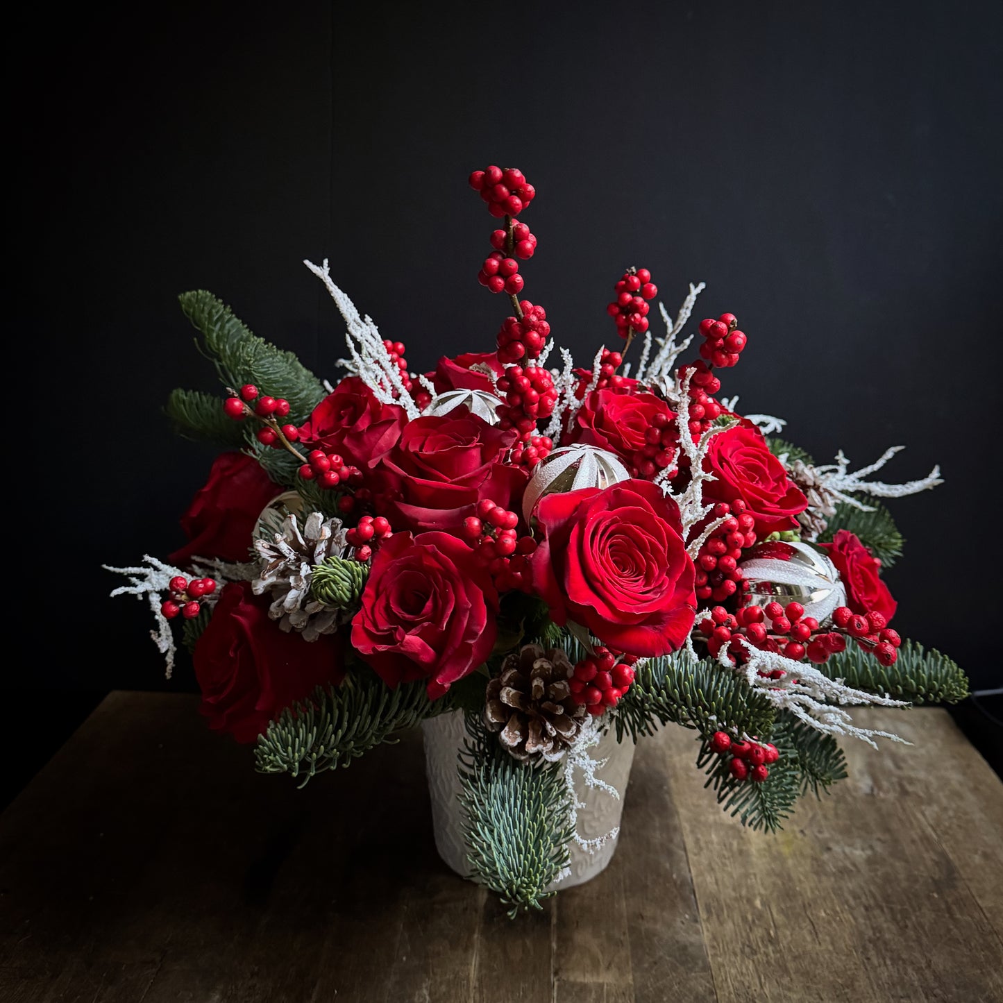 Alaric Flowers NYC Crimson Noël Centerpiece with red roses, winterberries, frosted branches & silver baubles, exuding festive, elegant warmth.