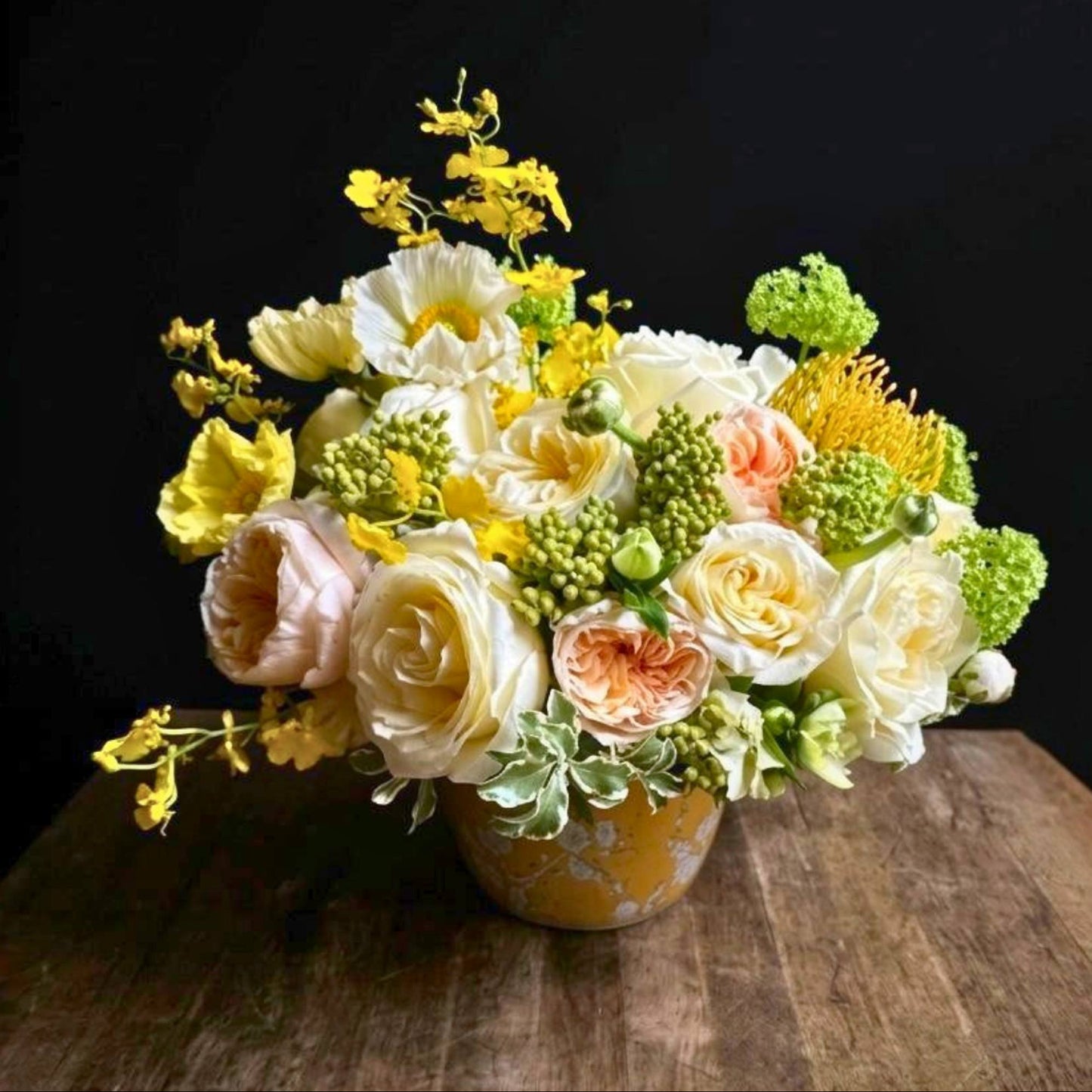 Bouquet of flowers in a yellow vase on a wooden surface with a black background