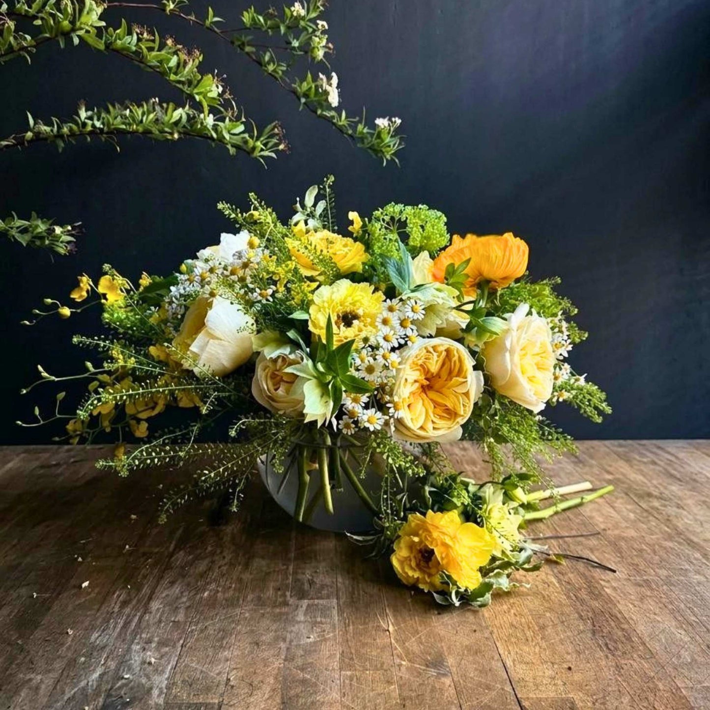 Bouquet of yellow and green flowers on a wooden table with a dark background
