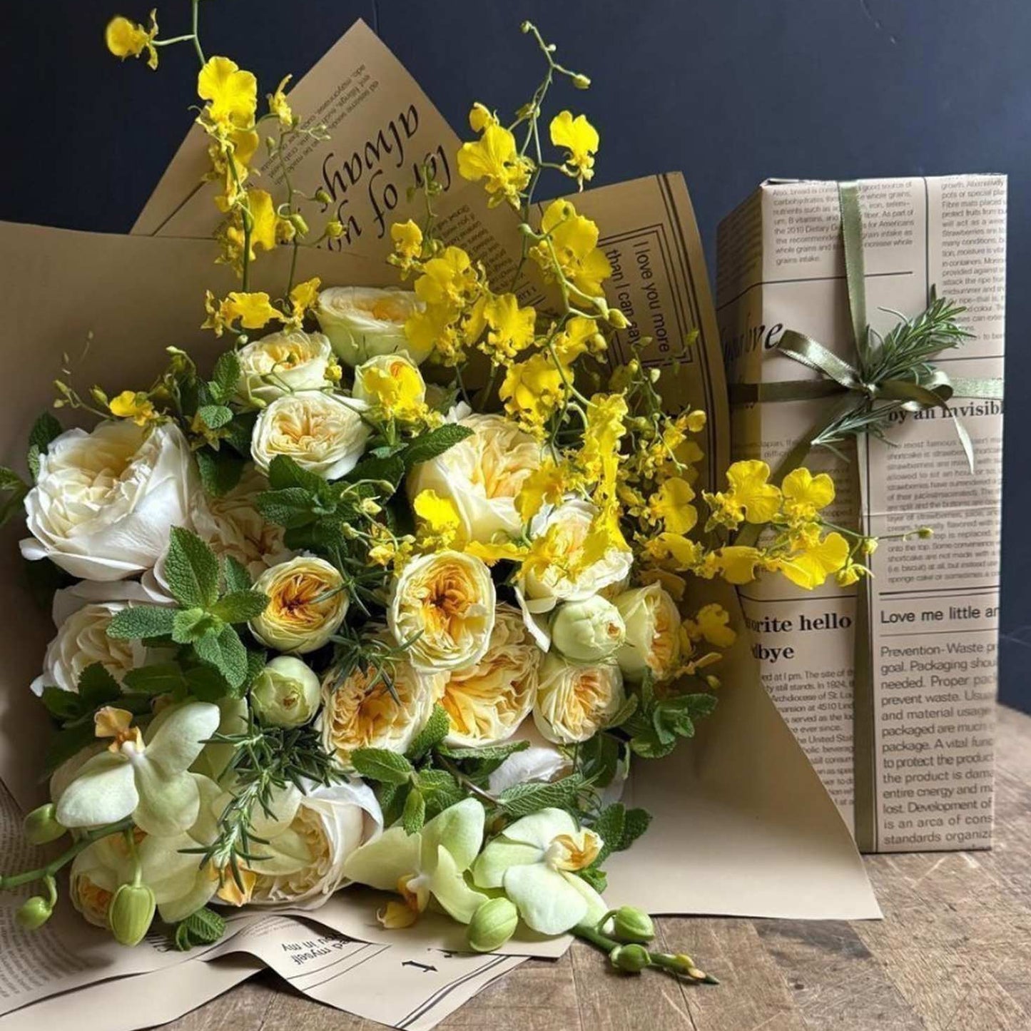 Bouquet of yellow and white flowers on a wooden surface with a wrapped gift box.