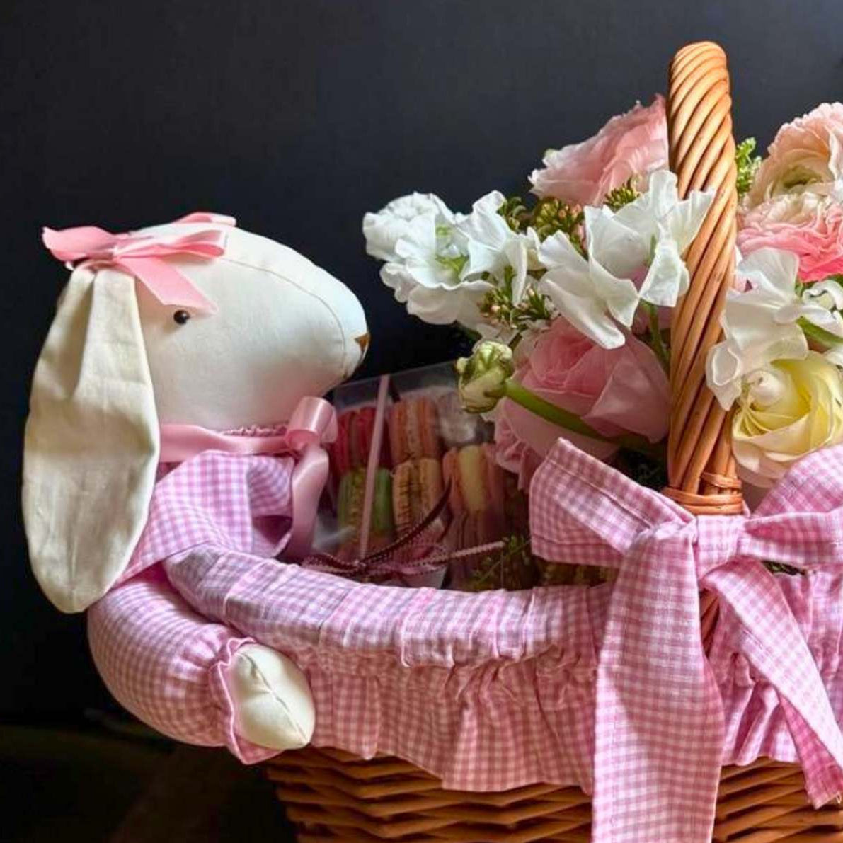 Wicker basket with flowers, a plush bunny, and candy on a wooden surface.