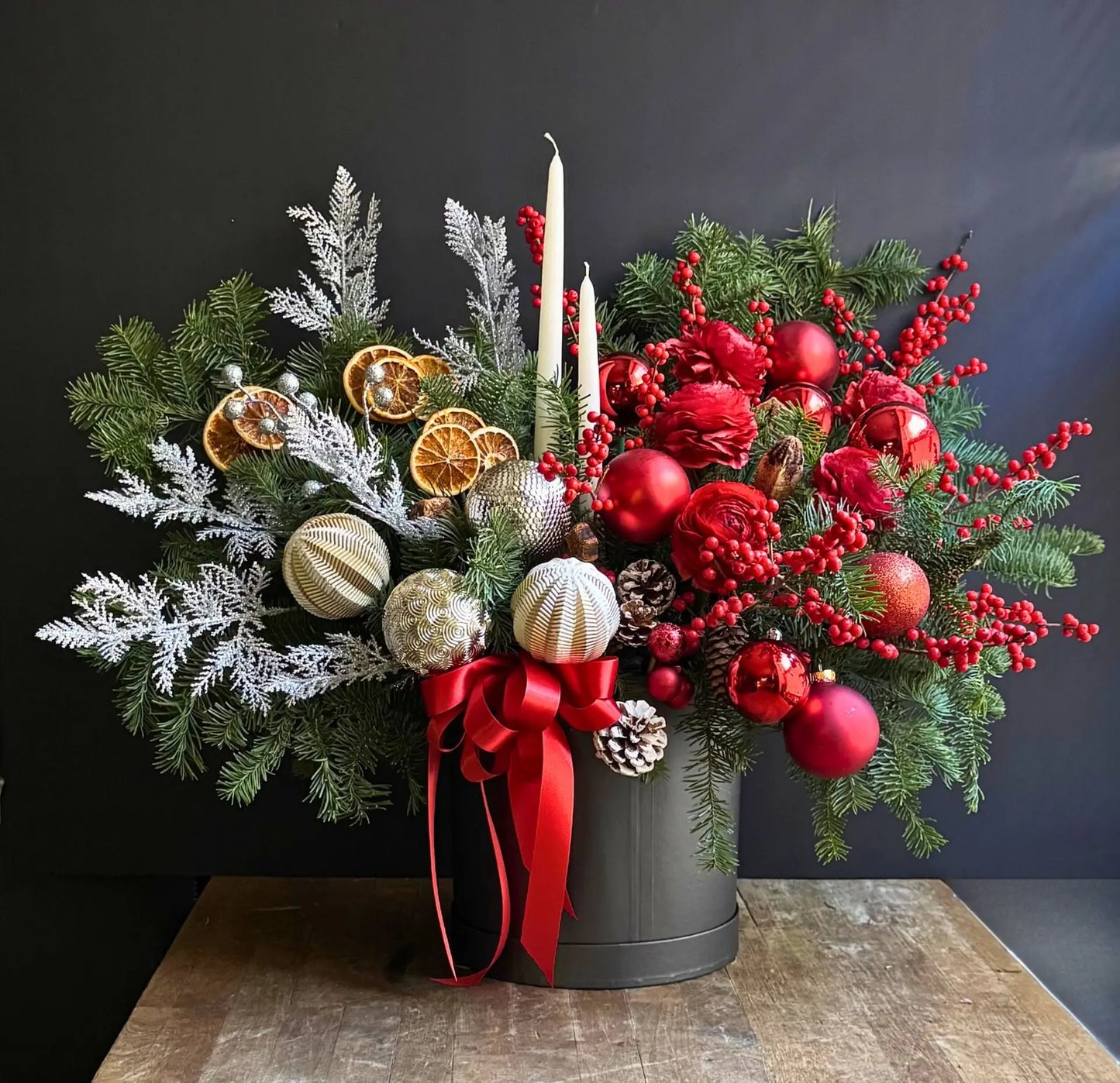 Alaric Flowers NYC Grand Holiday Luxe arrangement with red roses, winterberry branches, dried oranges, pine cones, metallic baubles, and candles.